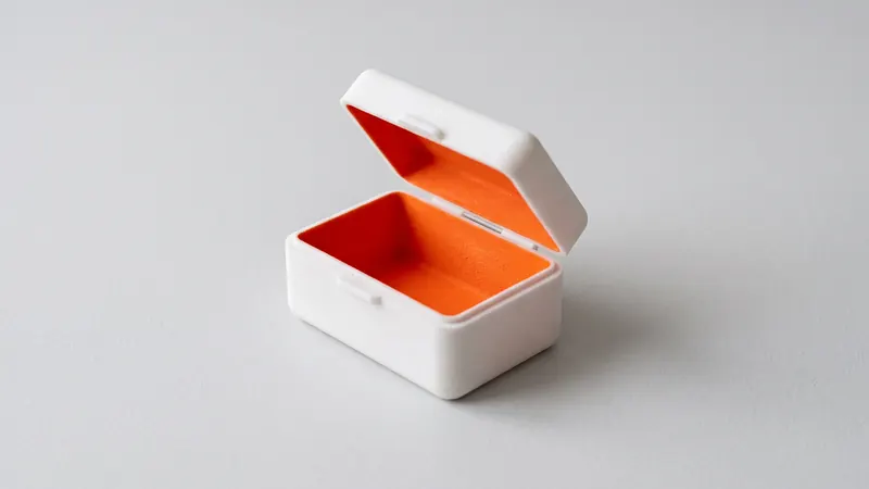 Kleine weiße SLS-Nylonbox mit halb geöffnetem Klappdeckel und orange gefärbtem Innenraum
